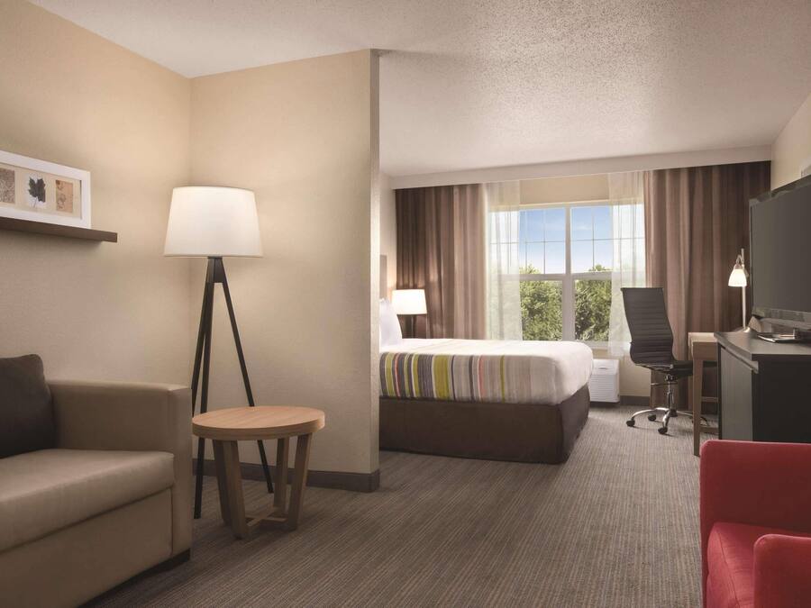 A hotel room with a bed, a desk, a chair, a small table, a sofa, a lamp, and a TV.