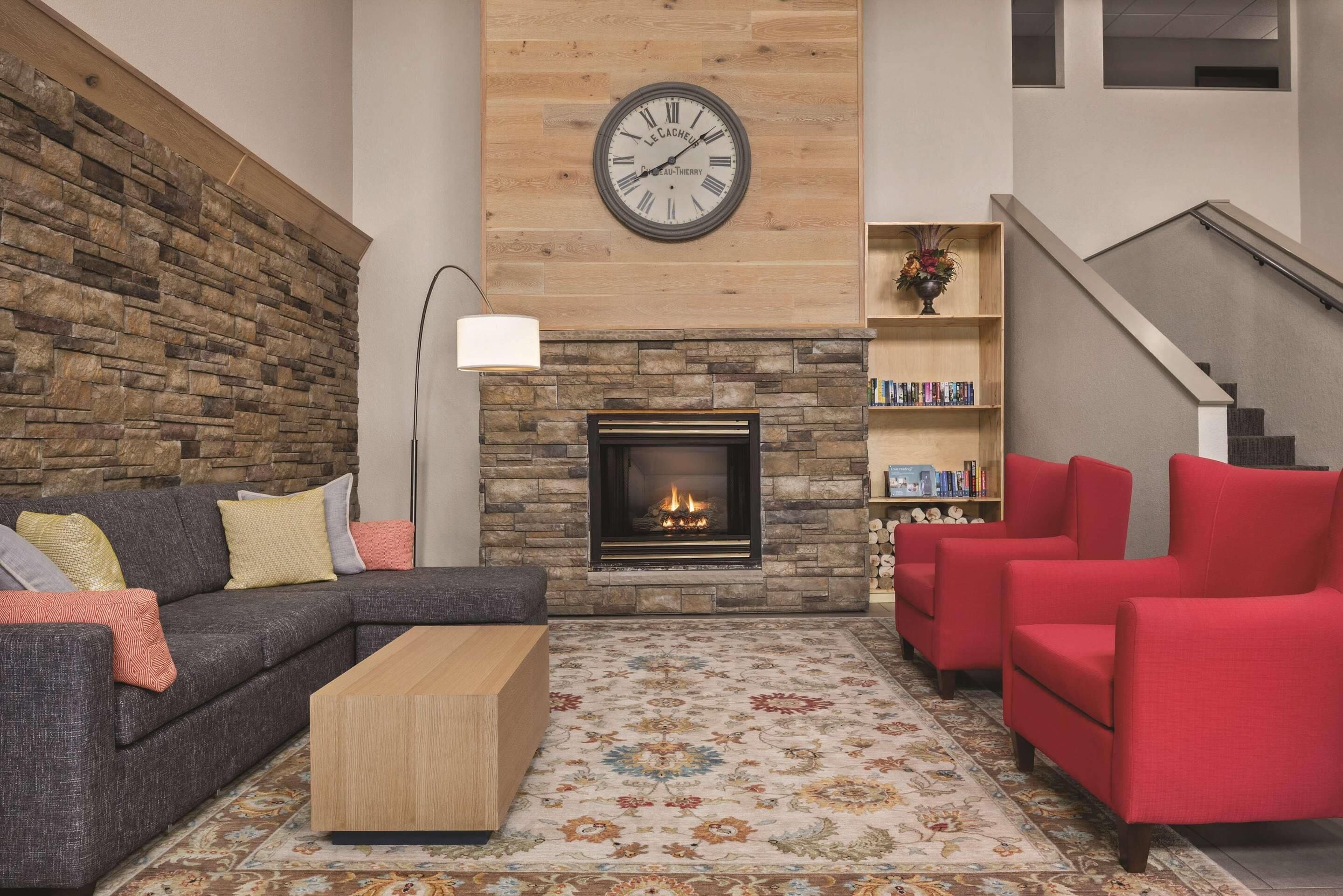 A living room with a stone wall, a fireplace, a clock, a sofa, a coffee table, and red armchairs.