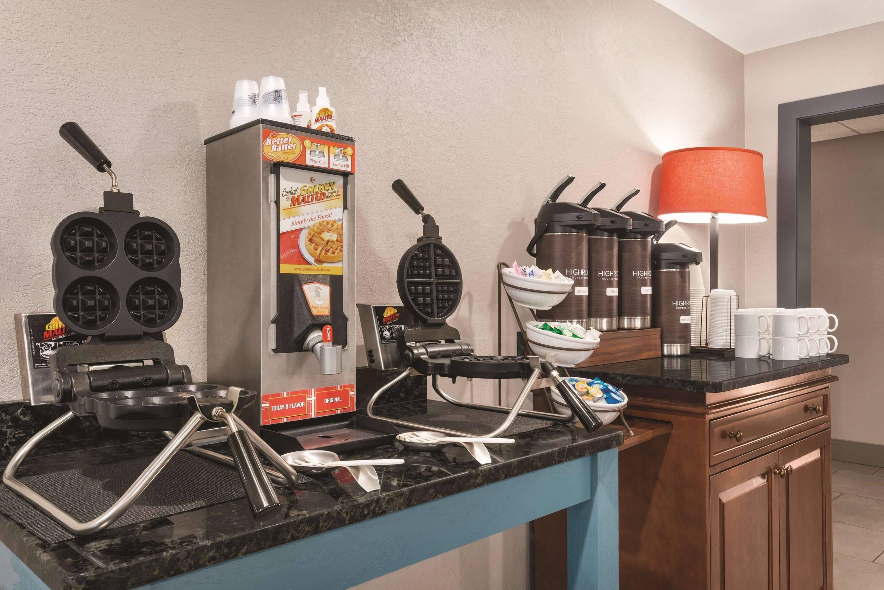 Eine Küchenzeile mit Waffelbuddel, einem Waffeleisen, einer Kaffeemaschine und einer Lampe.