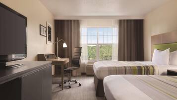 Habitación de hotel con una cama, un escritorio con computadora, una silla, televisor y ventana con cortinas.