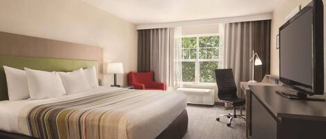 Habitación de hotel con una cama grande, un escritorio con computadora, televisor y ventana con cortinas.