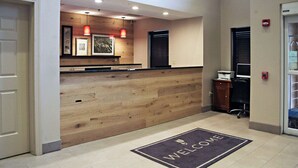 A reception area with a wooden reception desk, framed artwork on the wall, and a welcome mat. - Country Inn & Suites by Radisson, Frackville (Pottsville), PA (Pottsville)