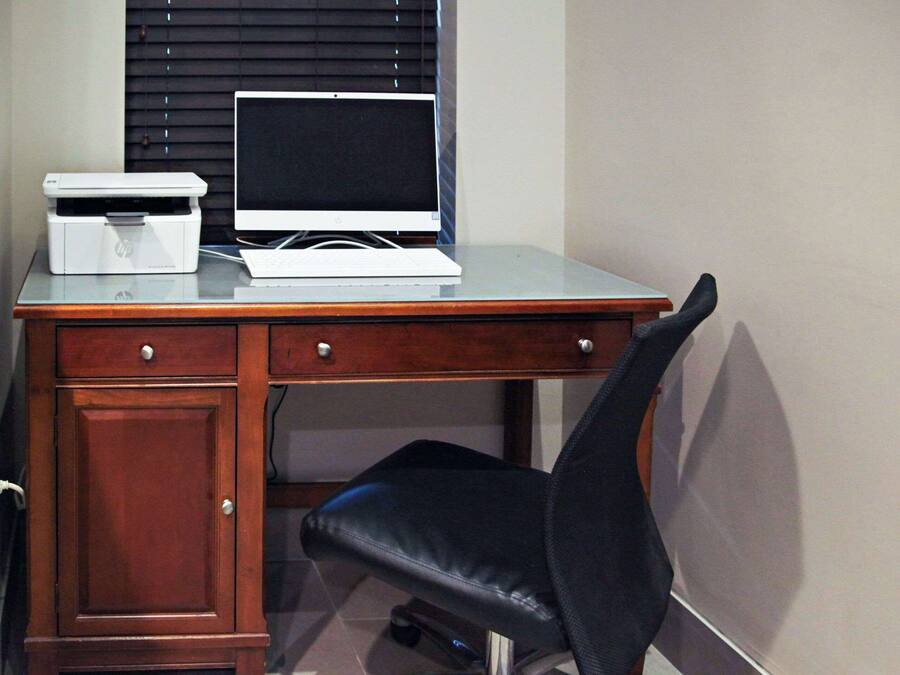 A wooden desk with a laptop, printer, and a black office chair.