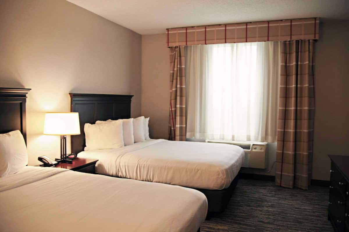 A hotel room with two beds, a nightstand with a lamp, a telephone, and a window with curtains.