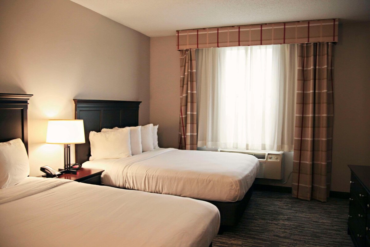 A hotel room with two beds, a nightstand with a lamp, a telephone, and a window with curtains.