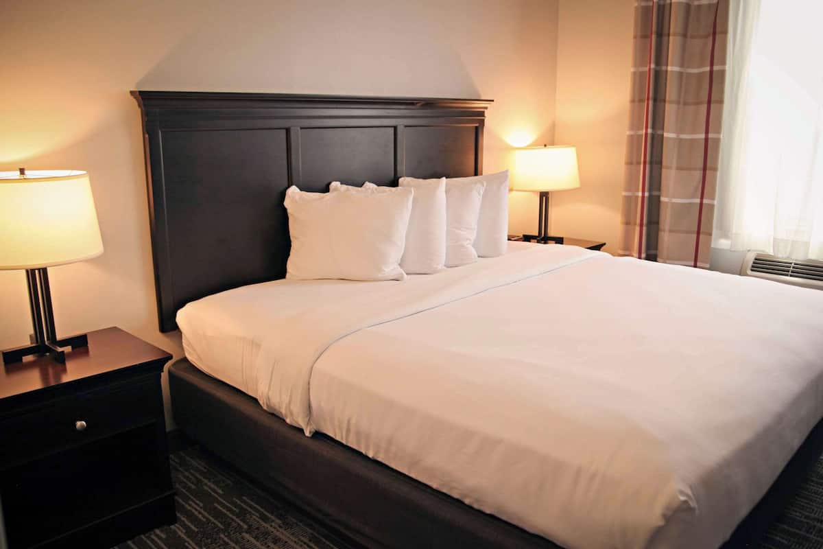 A hotel room with a large bed, dark headboard, two bedside tables with lamps, and a window with curtains.