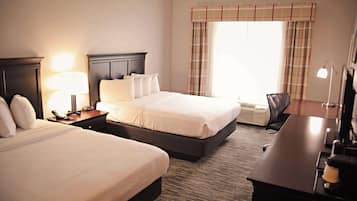 A hotel room with two beds, a desk, a lamp, a phone, and a window with curtains.