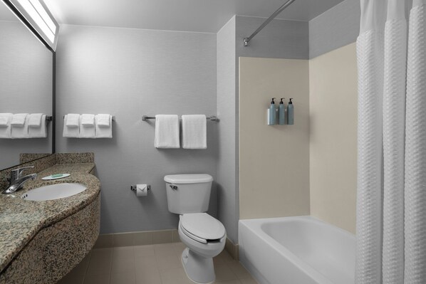 Une salle de bain avec un lavabo sur un plan de travail en granit, des toilettes, une baignoire et un rideau de douche.