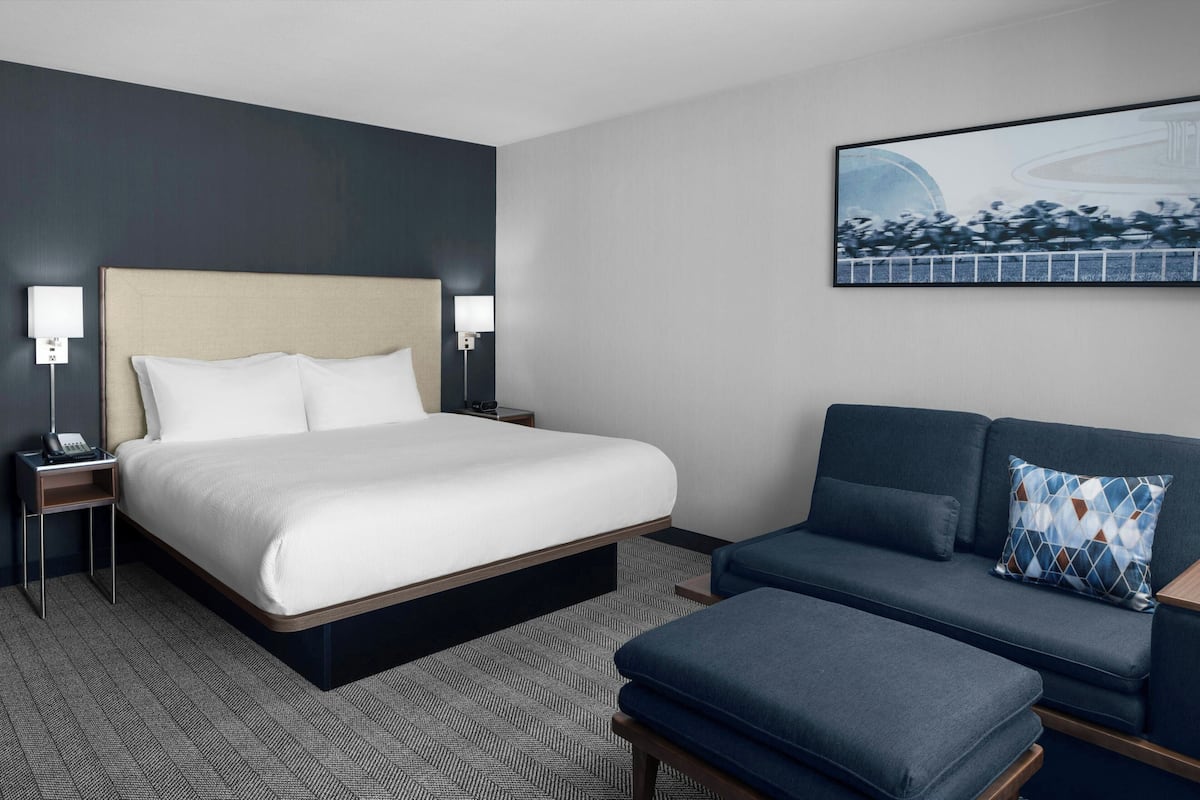 Ein Hotelzimmer mit Bett, Sofa, kleinem Tisch und einem an der Wand befestigten Fernseher.