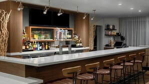 A modern bar area with a long counter, multiple stools, and a variety of liquor bottles.
