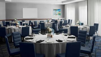 A conference room with round tables, blue chairs, and white tablecloths.
