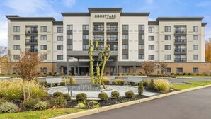 A multi-story hotel with a central courtyard, featuring a statue, benches, and landscaped gardens. - Courtyard by Marriott Philadelphia Langhorne (Langhorne)