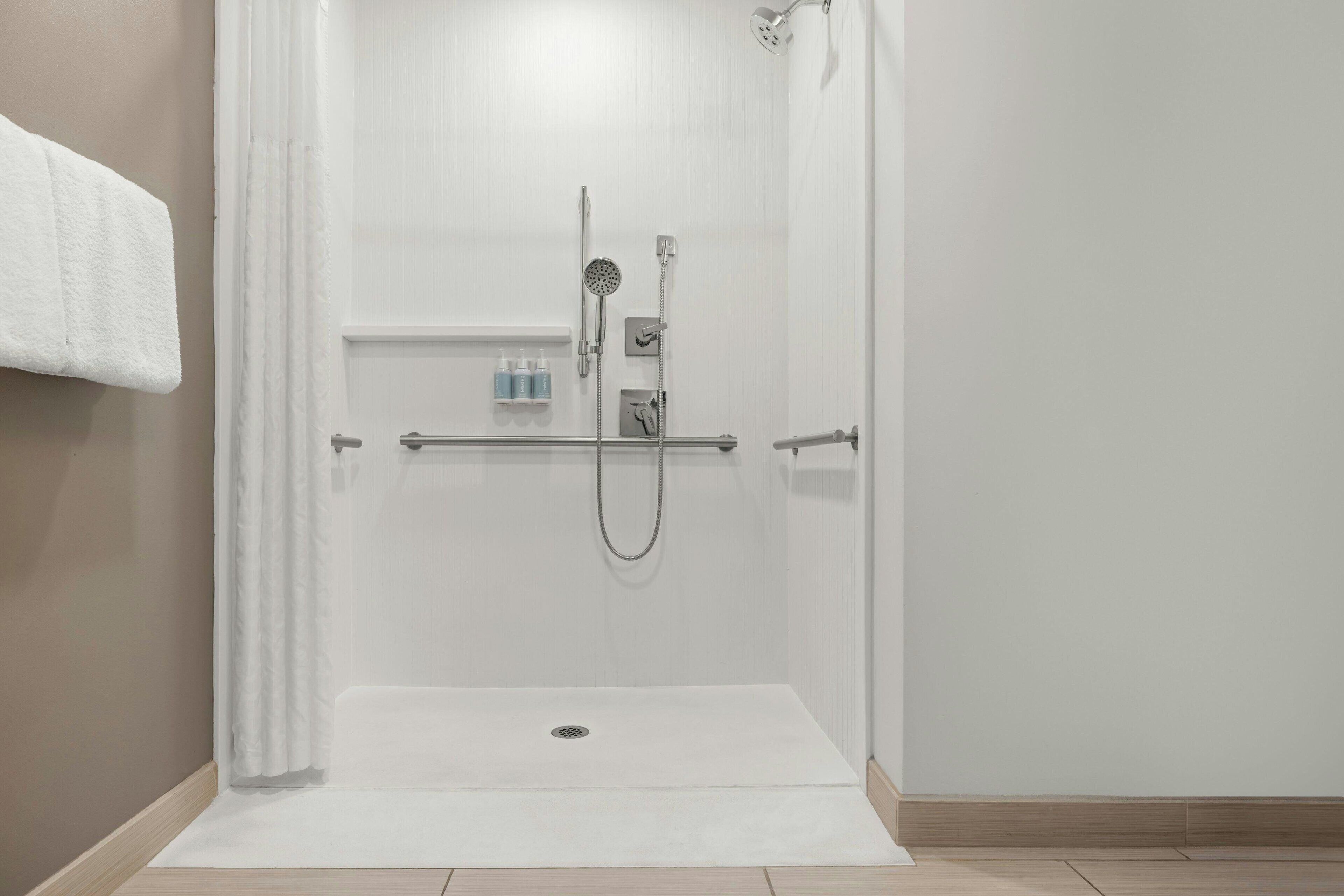 A walk-in shower with a glass door, a white towel hanging on the wall, and a shelf with toiletries.