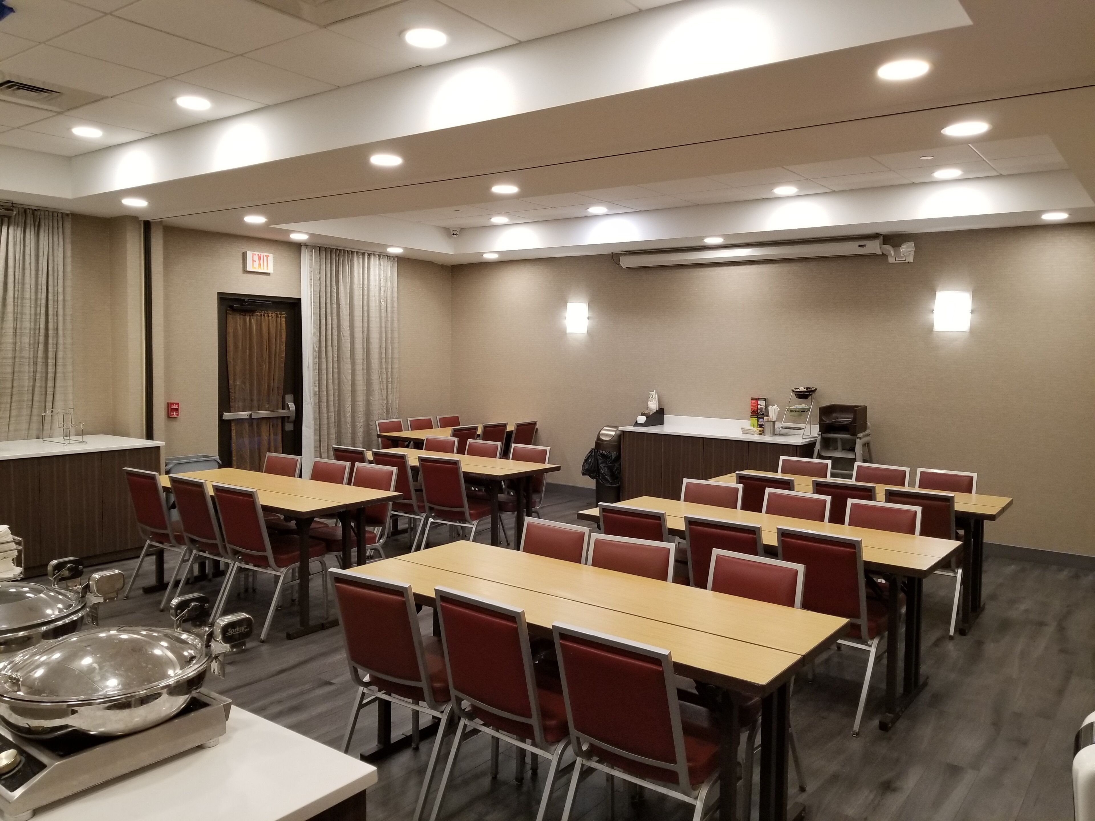 A conference room with multiple tables and chairs, an air conditioning unit, a reception desk, and an exit sign.
