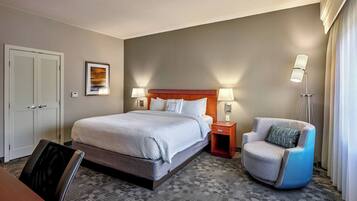 Una habitación de hotel con una cama grande, una silla, una mesita de noche y una lámpara.