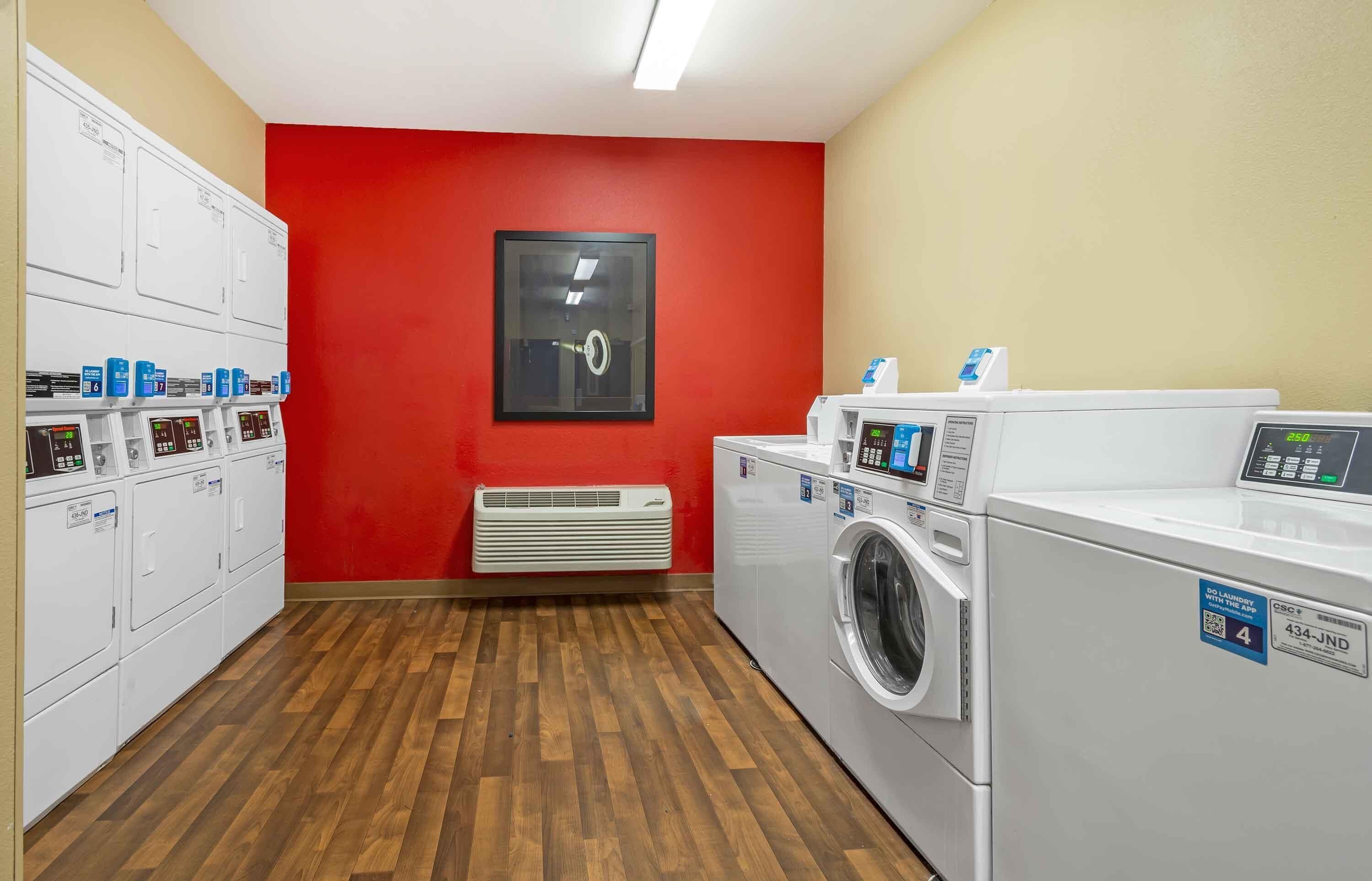 A laundry facility with multiple washing machines and dryers, a red wall, and a wooden floor.
