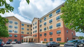 A multi-story hotel with a parking lot, a covered entrance, and a clear sky. - Extended Stay America Suites Secaucus Meadowlands (Secaucus)