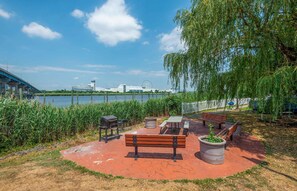 Un parque junto al lago con banco, mesa de picnic, parrilla y plantas en macetas.