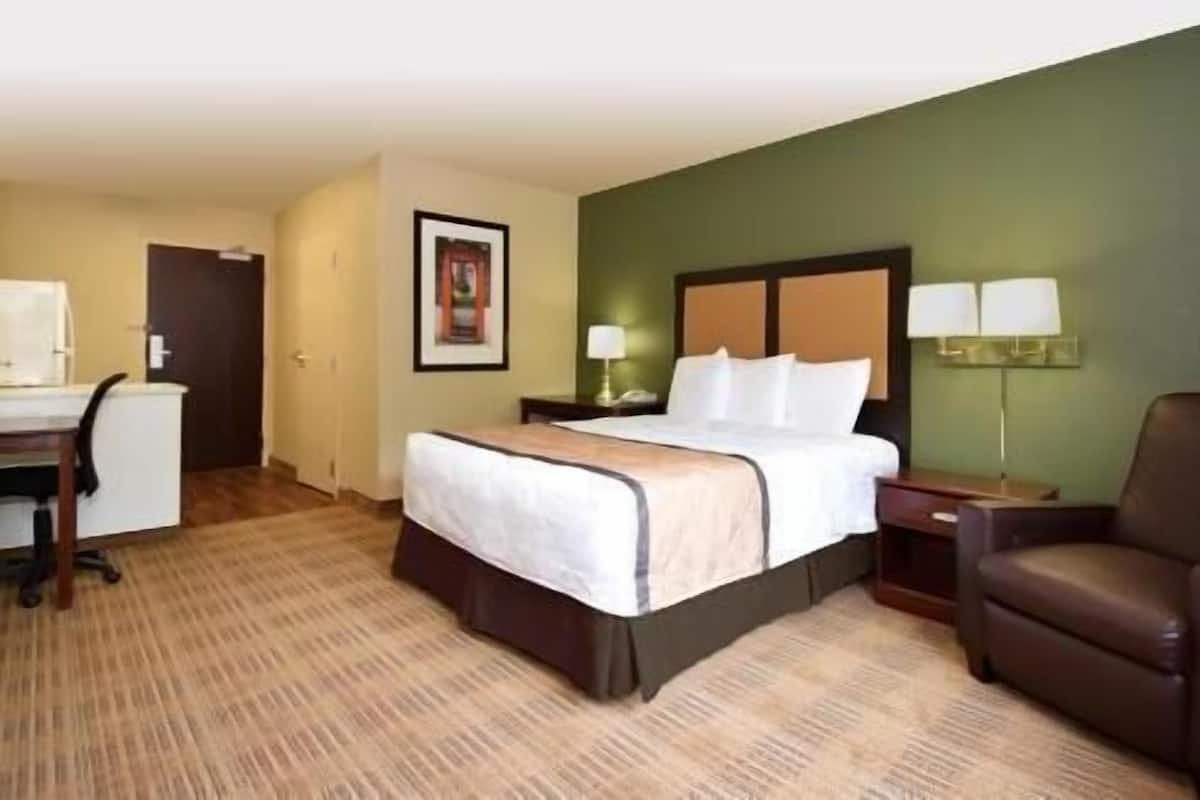 Una habitación de hotel con cama, escritorio, silla y un cuadro en la pared.