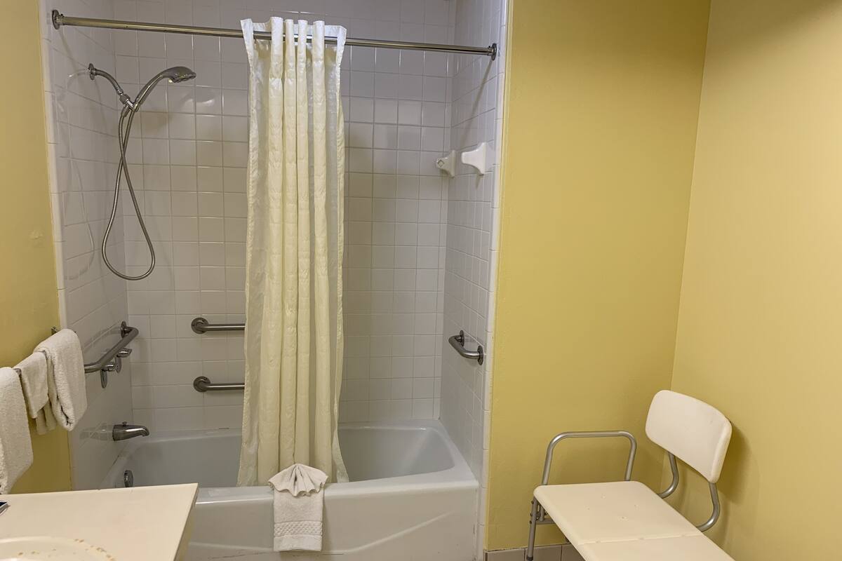 Un baño con ducha, bañera, inodoro y una mesita.