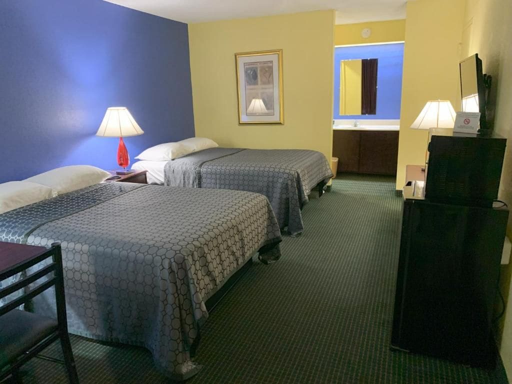 A hotel room with two beds, a desk, a chair, a TV, and a bathroom visible through an open door.