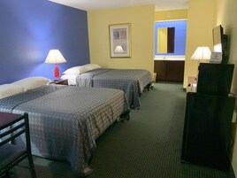 Habitación de hotel con dos camas, un escritorio, una silla, un televisor y un baño visible a través de una puerta abierta.