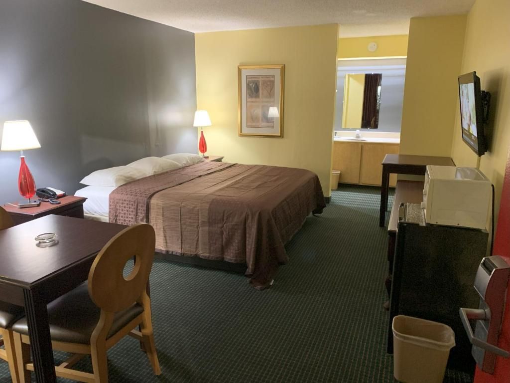 A hotel room with a bed, bedside table, lamp, chair, desk, and a television.
