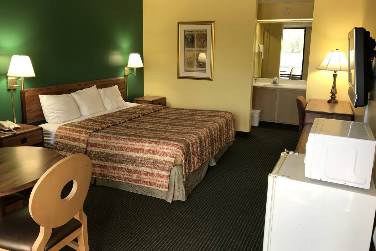 Habitación de hotel con cama, escritorio, silla, microondas y baño visible a través de una puerta abierta.