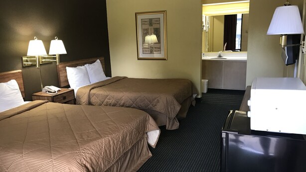 A hotel room with two beds, a desk, a lamp, a mirror, and a bathroom visible through an open door. - Relax Inn & Suites (Dublin)