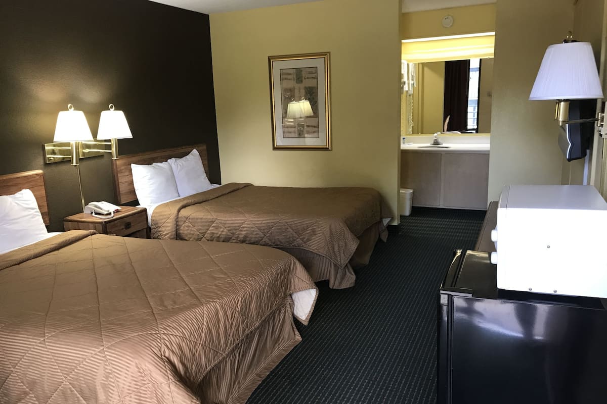 Habitación de hotel con dos camas, un escritorio, una lámpara, un espejo y un baño visible a través de una puerta abierta.