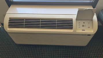 Een staande airconditioner met bedieningspaneel, in een kamer met raam en een vloerkleed met dessin.