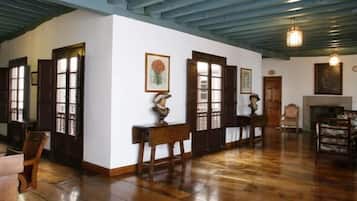 A spacious room with wooden flooring, a high ceiling with exposed beams, and a fireplace. There are several wooden doors and a bench along the wall.
