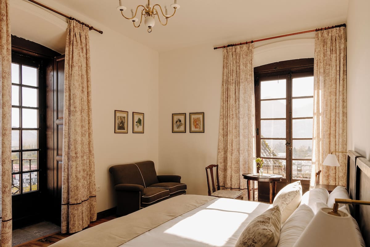 Quarto com cama, sofá, cadeira, mesa e janela com cortinas.