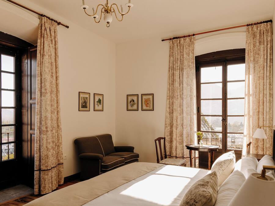 Una habitación con cama, sofá, sillón, mesa y ventana con cortinas.