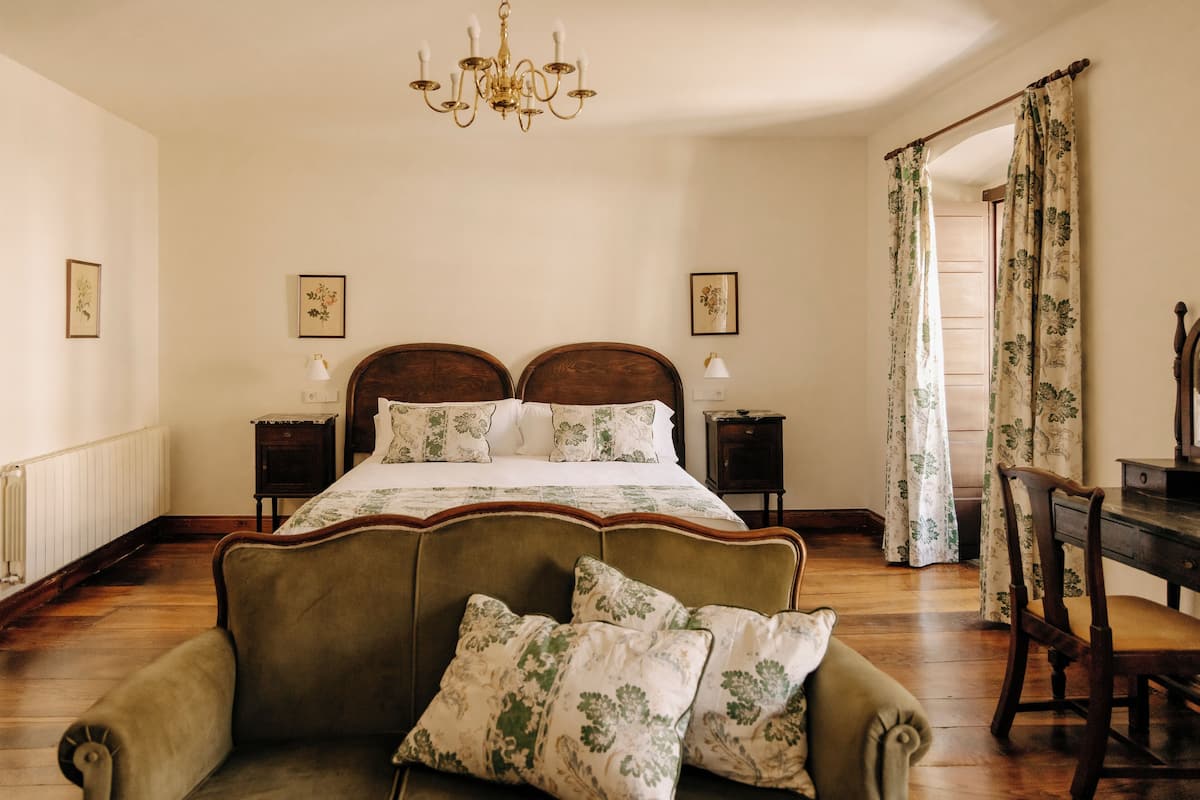 Quarto com uma cama grande, duas mesas de cabeceira, um lustre e cortinas florais.