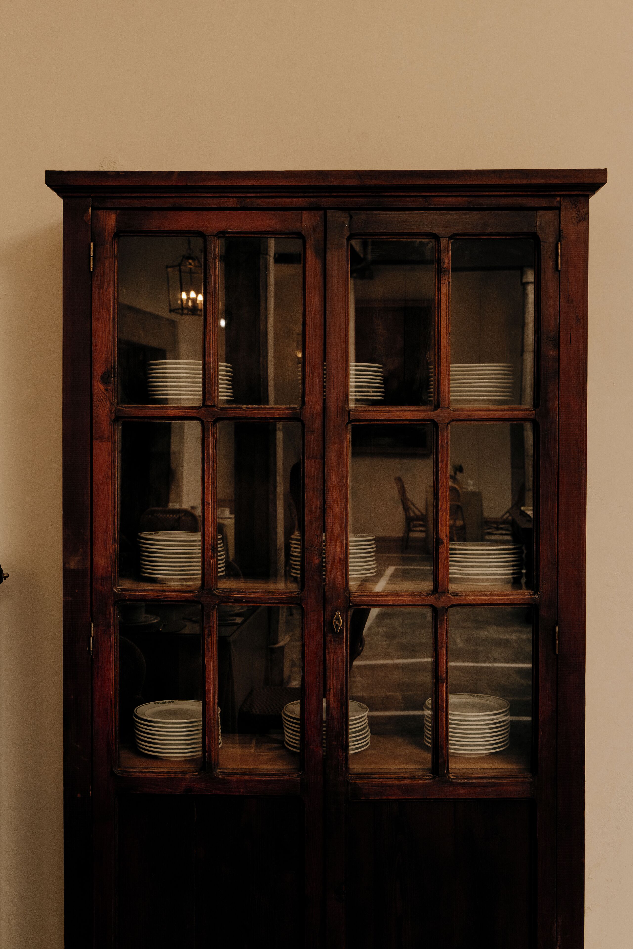 A wooden cabinet with glass doors containing stacked plates.