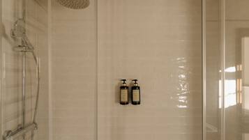 A shower with a handheld showerhead and two bottles of shampoo on the wall.
