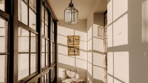 A narrow hallway with large windows, a chair, and a hanging light fixture. - Hotel PAX Casona del Busto (Pravia)