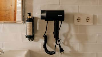 Un bagno con un lavandino bianco, uno specchio, uno scaffale in vetro con tazze, un asciugacapelli e una bottiglia di shampoo.