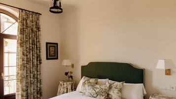 Una cama bien hecha con un cabecero verde, dos mesitas de noche con lámparas, una ventana con cortinas estampadas y un cuadro colgado en la pared.