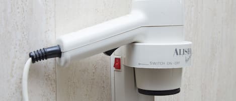 A white hair dryer with a switch and a red button, mounted on a wall.
