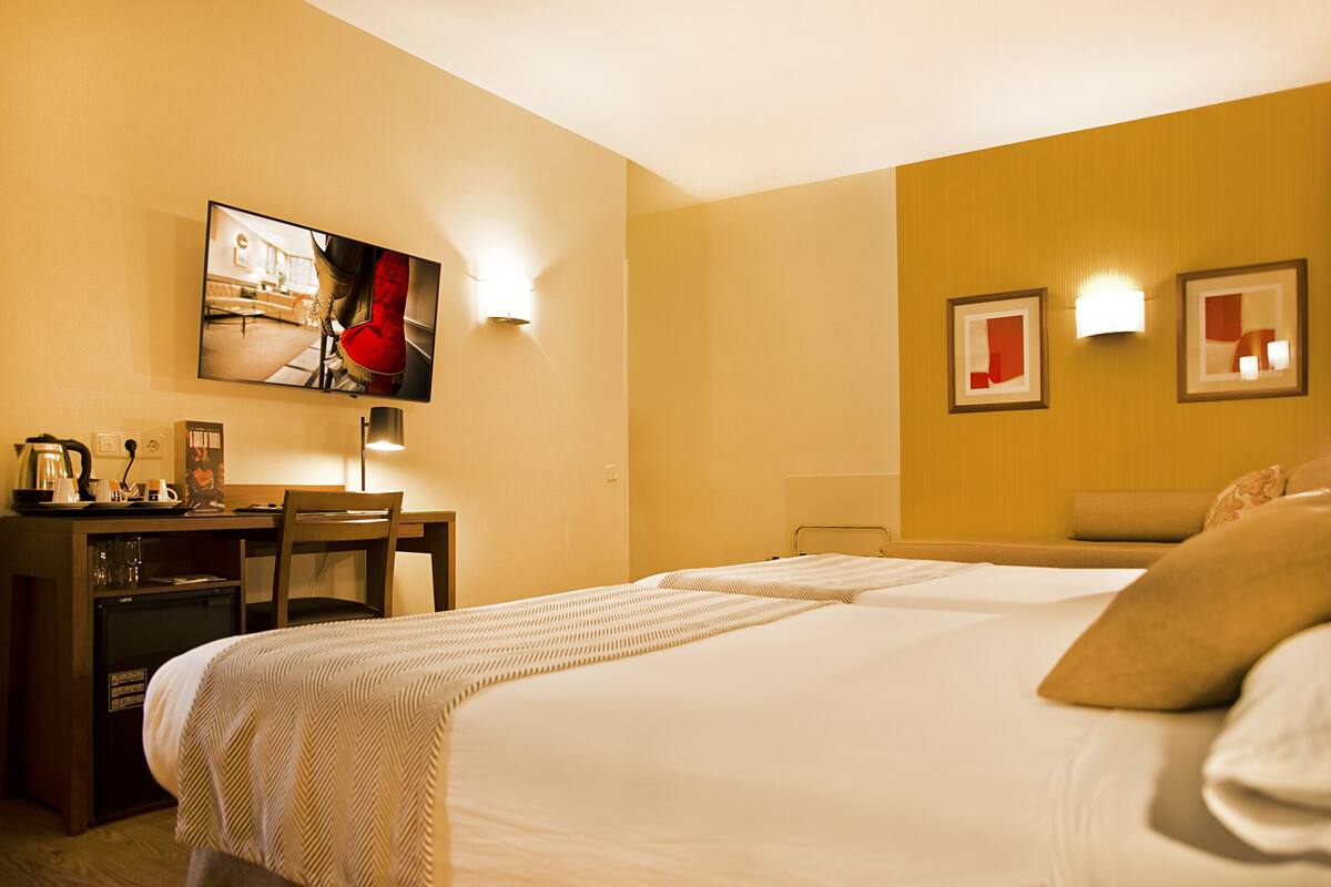 A hotel room with a bed, desk, chair, and a television on the wall.