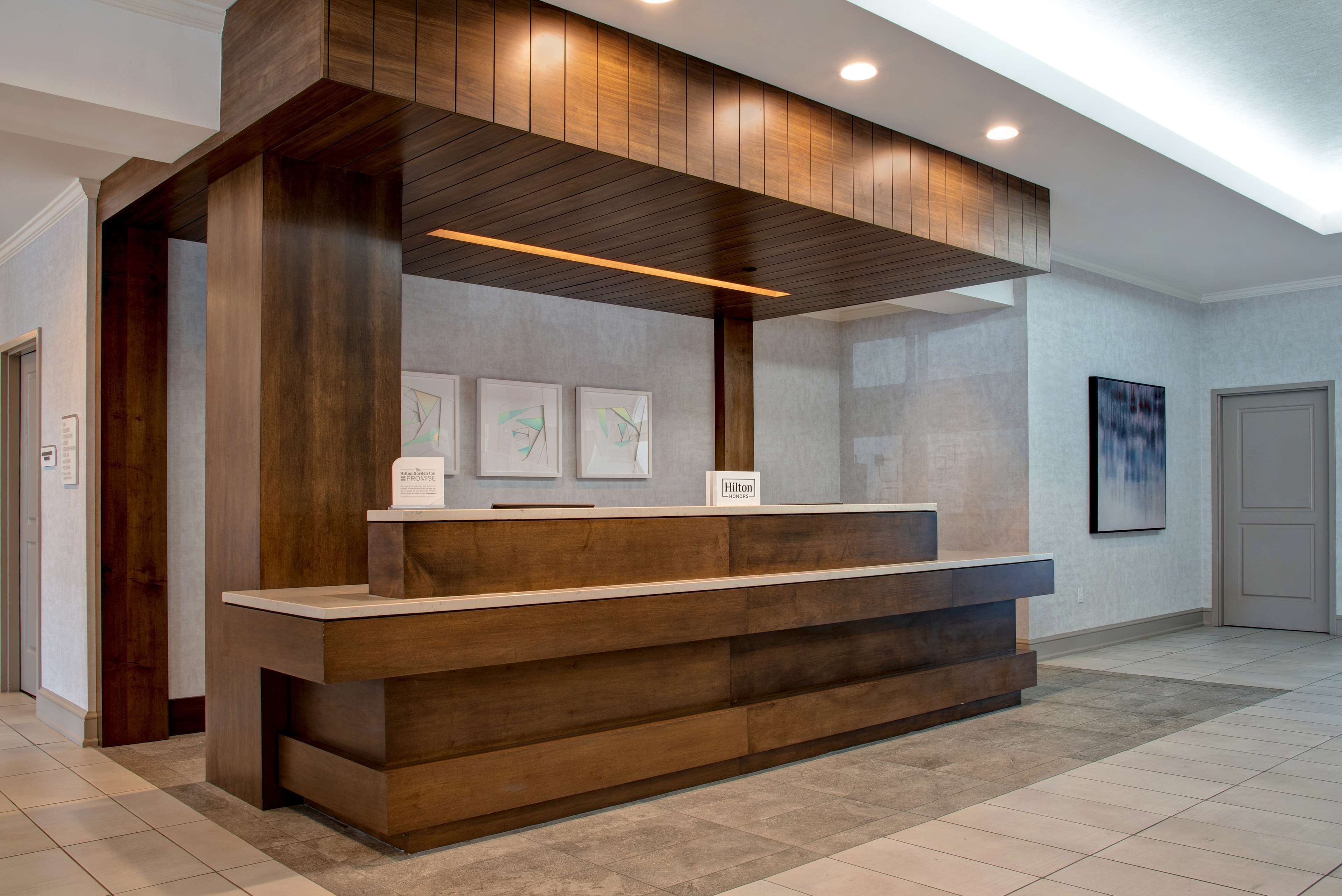 A reception desk with a wooden finish, a sign indicating it's a Hilton hotel, and framed artwork on the wall.