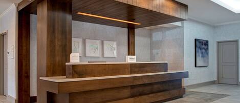 A reception desk with a wooden finish, a sign indicating it's a Hilton hotel, and framed artwork on the wall.