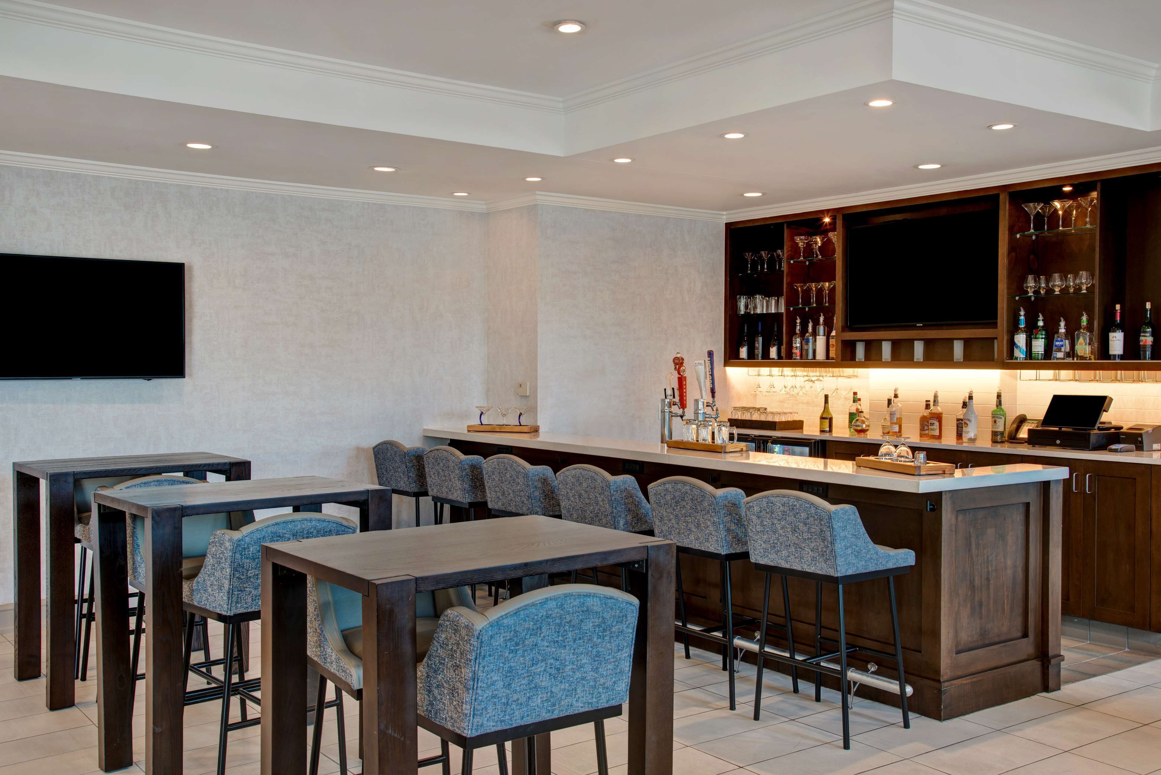 A bar area with a long counter, multiple bar stools, and a television mounted on the wall.