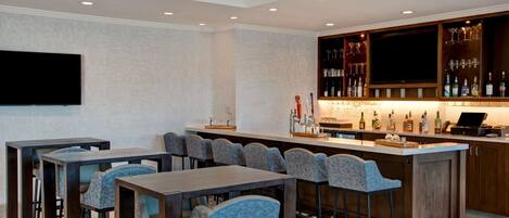 A bar area with a long counter, multiple bar stools, and a television mounted on the wall.