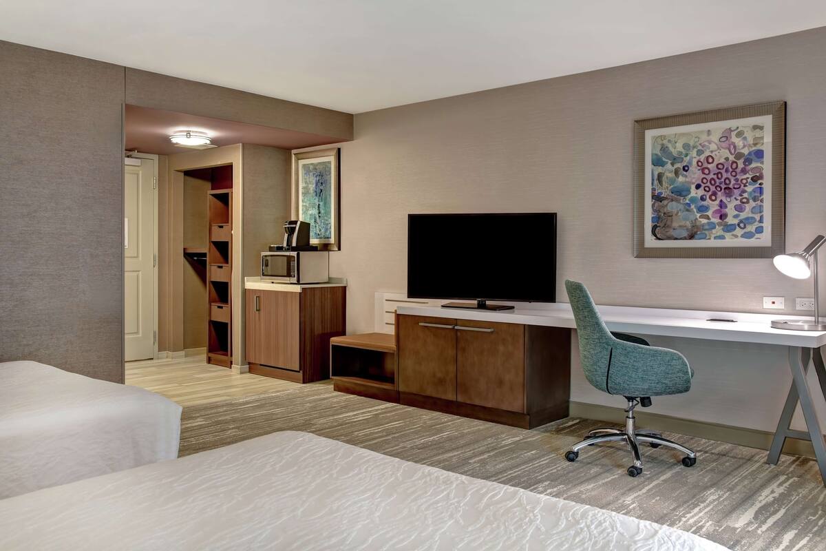 A hotel room with a bed, a desk with a chair, a television, and a wardrobe.