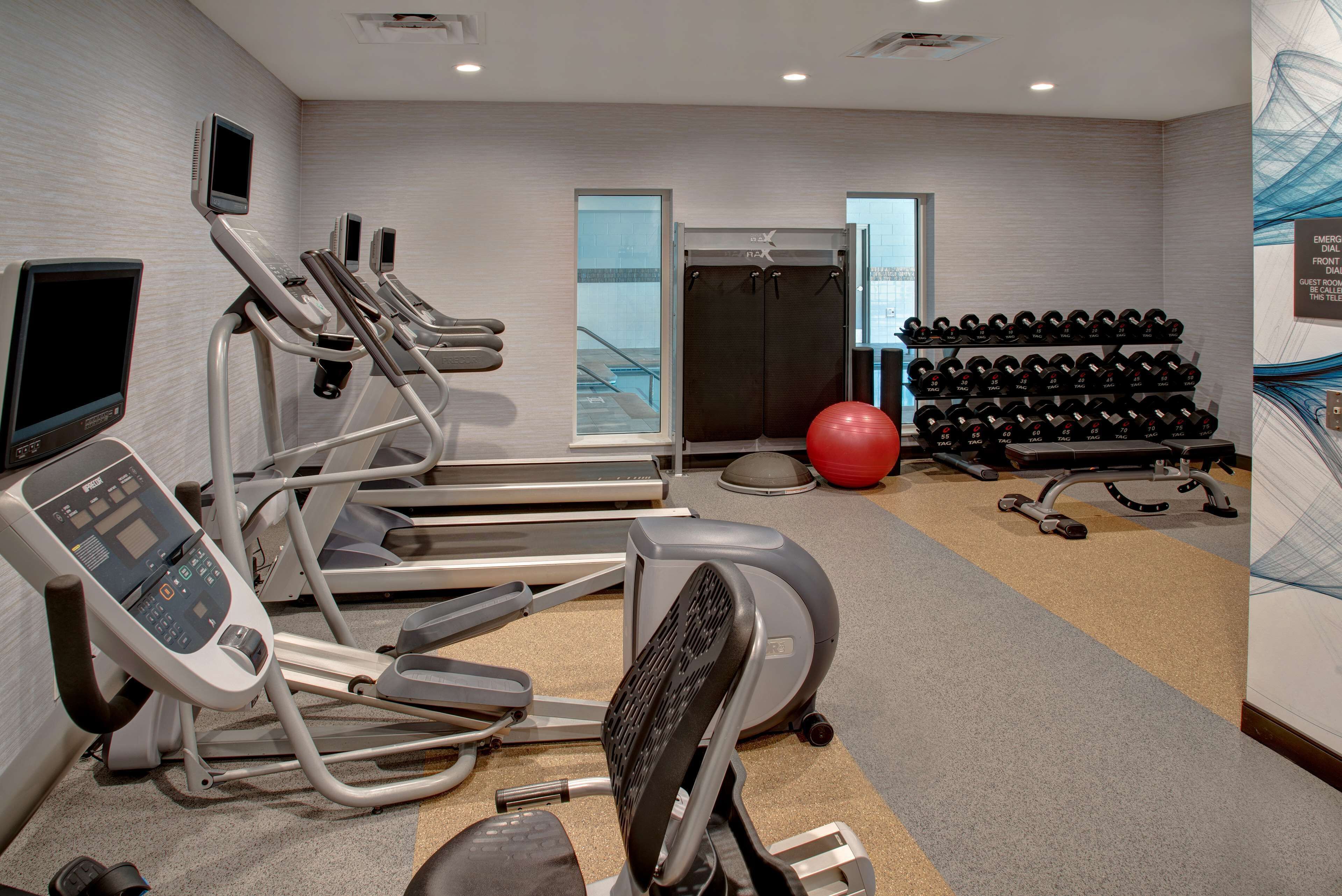 A gym with treadmills, ellipticals, a red exercise ball, and a rack of dumbbells.