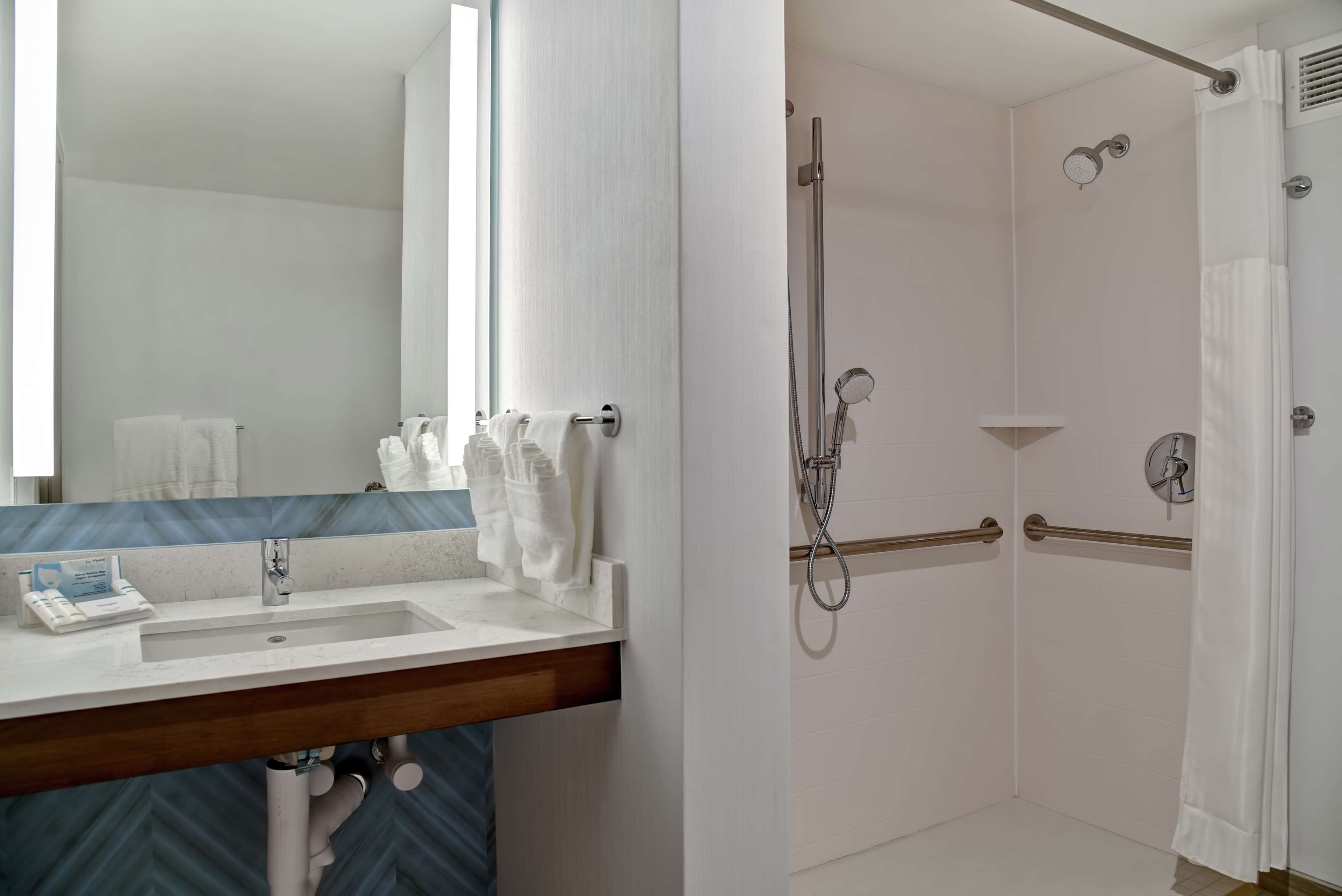 A bathroom with a sink, mirror, and shower area.