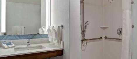 A bathroom with a sink, mirror, and shower area.